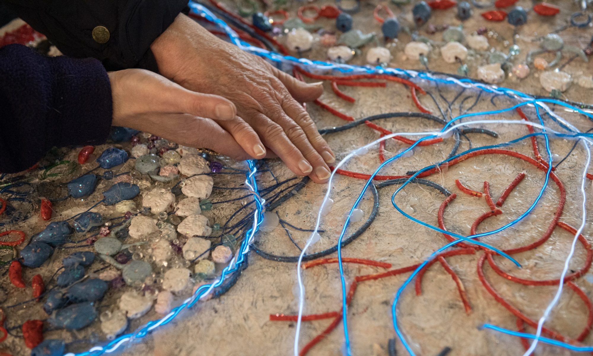 Guiding hands over Tactile Retina Map braille inspired map of retinal cells art work by Erica Tandori, Photography by Hynesite Photography